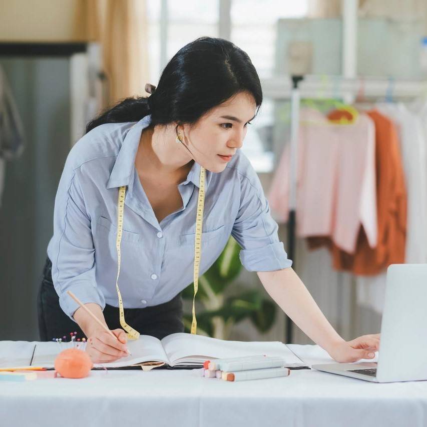 Diseñador de moda femenina mirando laptop con cinta métrica amarilla alrededor del cuello
