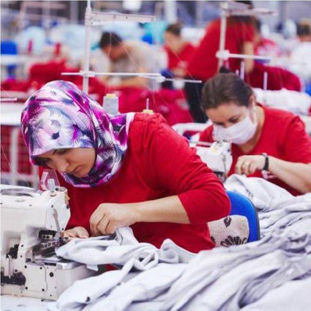 Mujer con colorido pañuelo en la cabeza usando una máquina de coser en fábrica