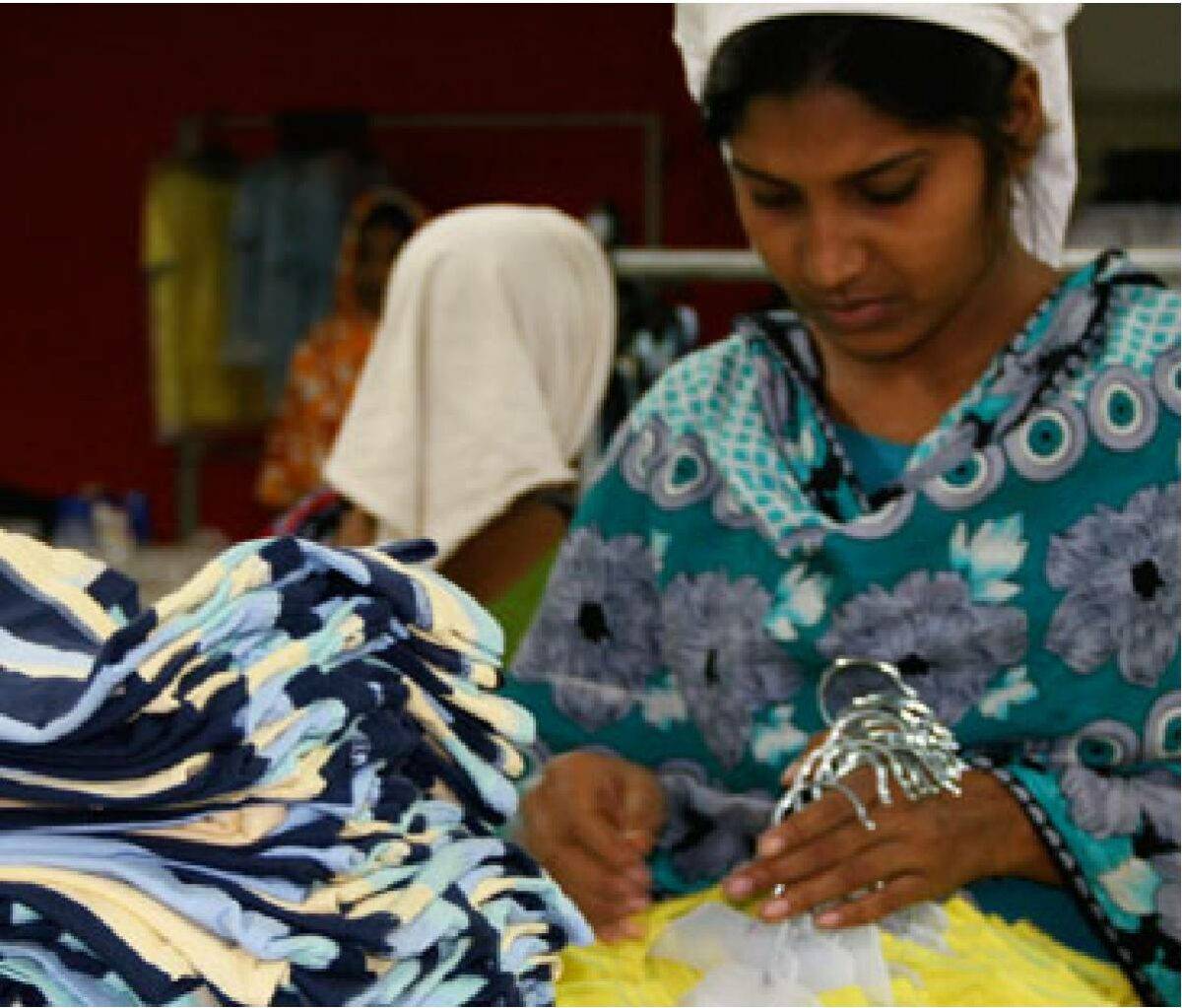 Female Epyllion employee looking at blue and yellow garments in garment factory