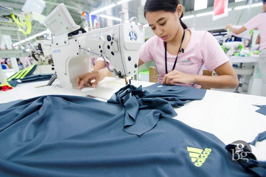 Female Apparel One seamstress sewing blue addidas t-shirt on sewing machine