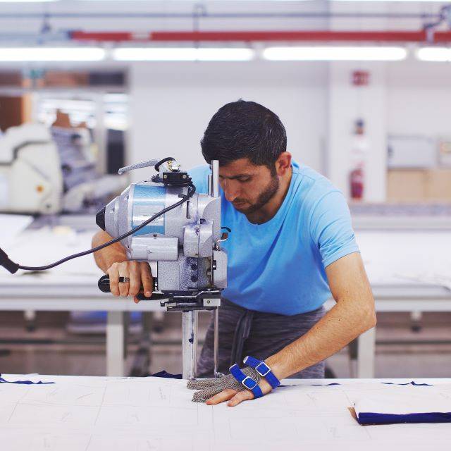 戴防护手套的男子在工厂用机器切割布料
