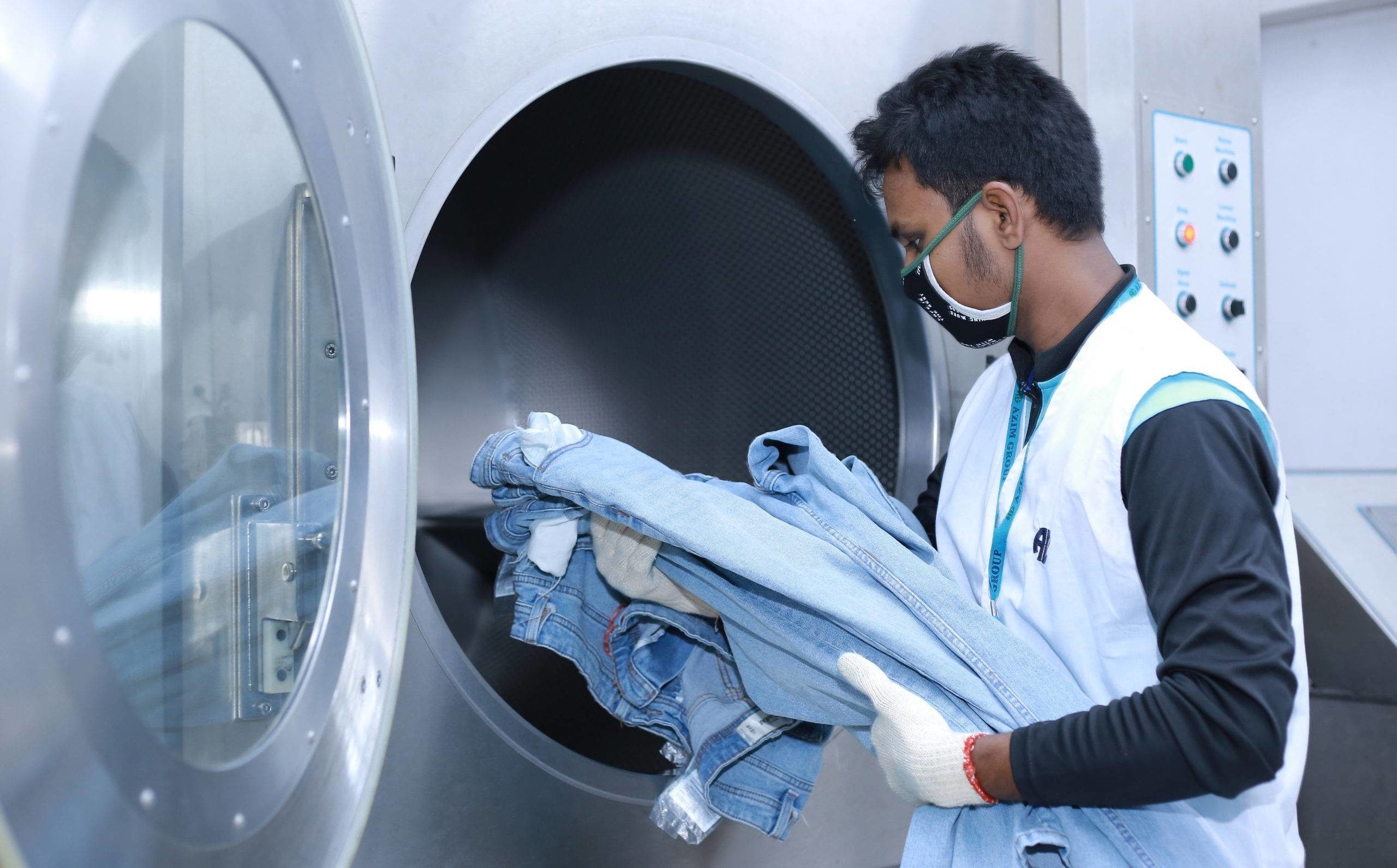 Garment factory worker putting denim jeans inside an industrial washing machine for laundry