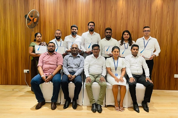 Winterquilt's Group photo of 12 certificate recipients and attendees posing in a wood-paneled room after a recognition or GSDCost training completion event.